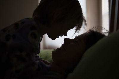 Silhouette mother and daughter looking at each other while relaxing on bed at home