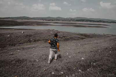 Rear view of man standing on mountain against sky