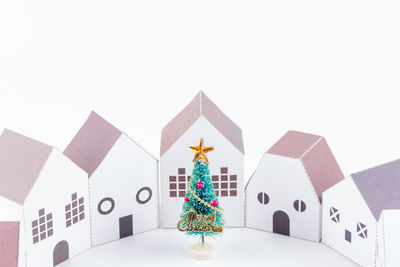 Close-up of christmas tree with model houses against white background