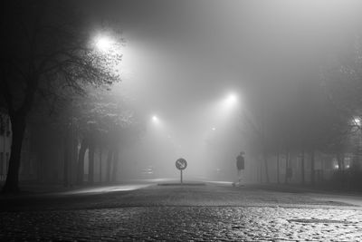 Full length of man walking on illuminated cobbled street at night during foggy weather