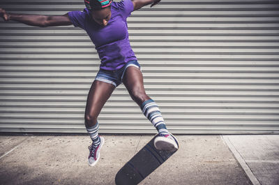 Full length of woman skateboarding against shutter