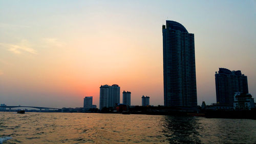 Sea by buildings against sky during sunset