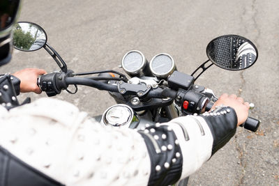 Crop male biker in black leather jacket and helmet riding modern motorbike on asphalt road amidst lush green trees growing in mountainous valley