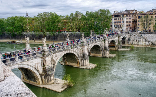 Arch bridge over river in city against sky
