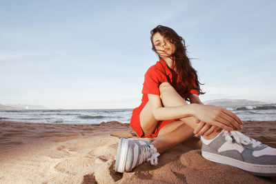 Young woman sitting on beach against sky