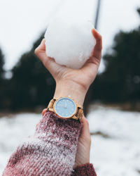 Close-up of hand holding clock against blurred background