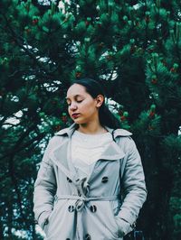 Beautiful young woman looking away against trees