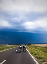 People riding bicycle on road against cloudy sky