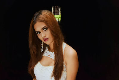 Portrait of young woman standing against black background