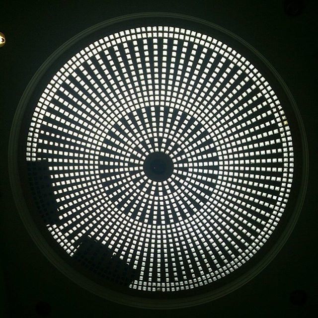 indoors, low angle view, circle, geometric shape, window, glass - material, ceiling, pattern, skylight, architecture, built structure, design, directly below, illuminated, transparent, shape, lighting equipment, sky, no people, modern