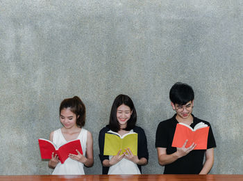 Friends reading while sitting by table against wall in classroom