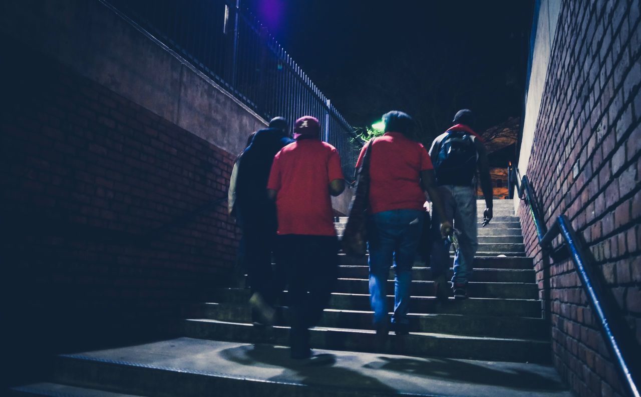 REAR VIEW OF MEN WALKING ON STEPS AT NIGHT