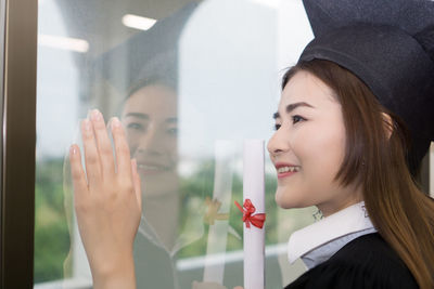 Young woman in graduation gown standing by glass window