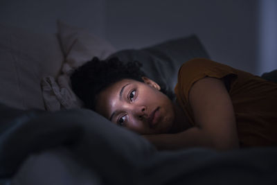 Pensive young woman lying in bed