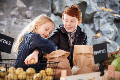 Smiling male and female sibling buying vegetables at market stall