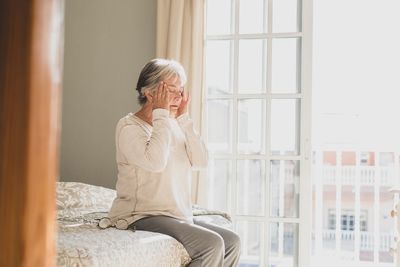 Senior woman sitting on bed at home by window