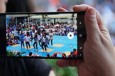 Cropped hand videographing people through smart phone