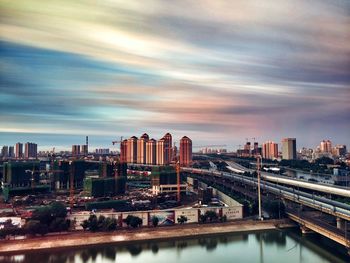 Bridge over river in city against dramatic sky