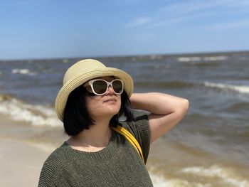 Young woman wearing hat while standing at beach against sky