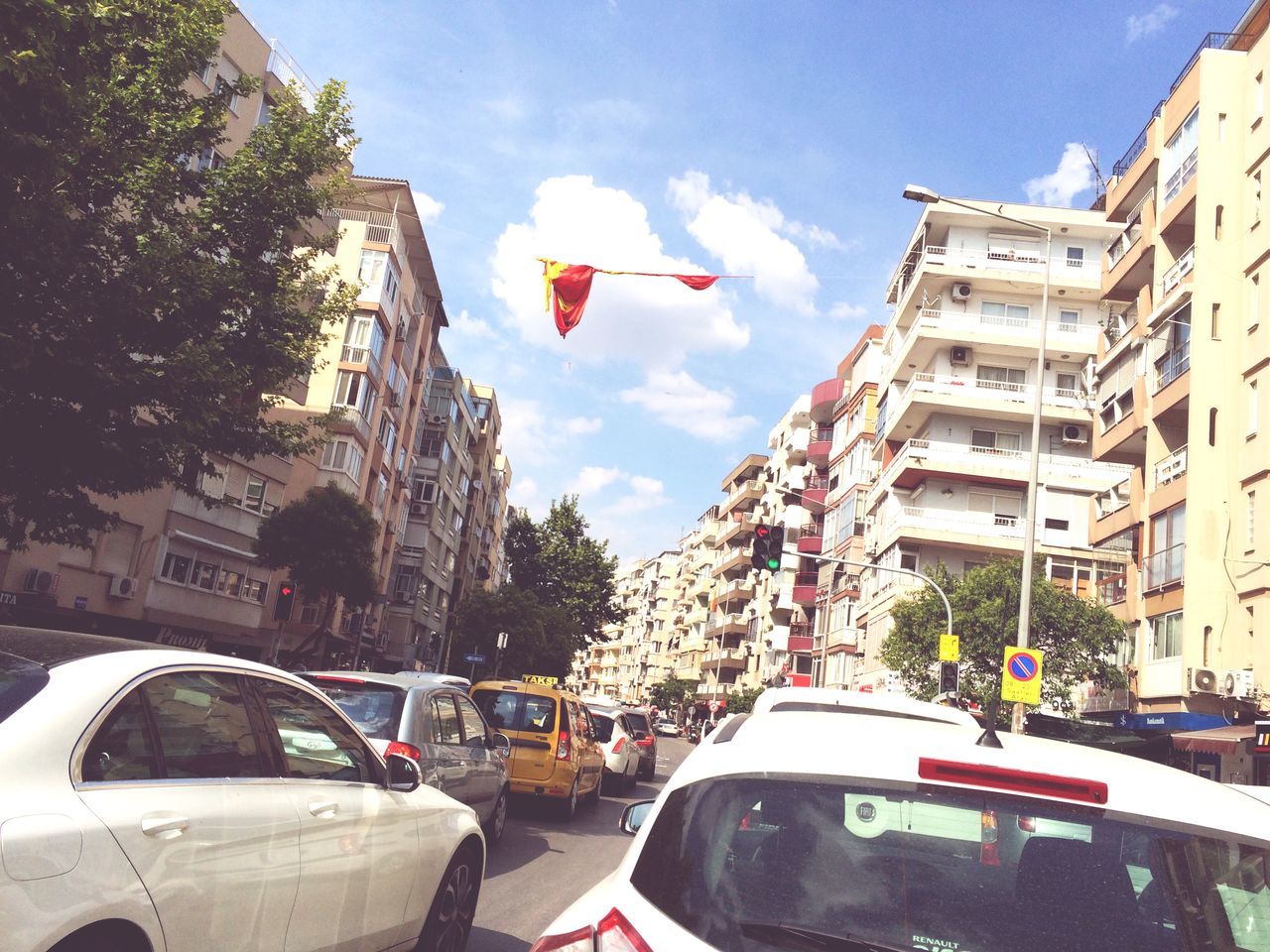 building exterior, transportation, architecture, mode of transport, built structure, car, land vehicle, flag, city, sky, street, road, patriotism, national flag, cloud - sky, day, cloud, travel, city street, city life