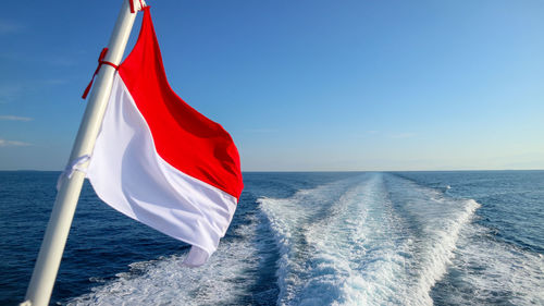 Scenic view of flag on sea against blue sky