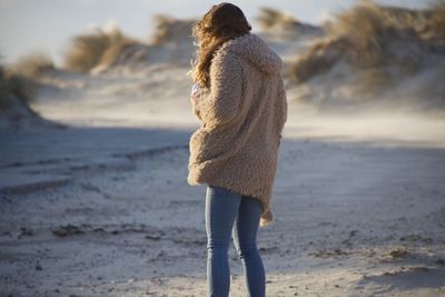 Rear view of woman wearing fake fur standing on beach