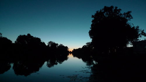 Silhouette trees by lake against clear sky during sunset