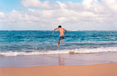 Full length of man jumping on beach against cloudy sky