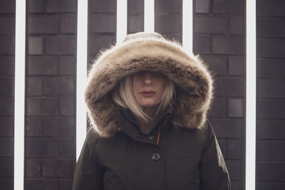 Close-up woman in hooded clothing standing against illuminated lights on wall