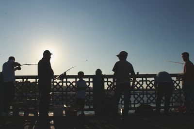 Silhouette people standing by railing against sky during sunset