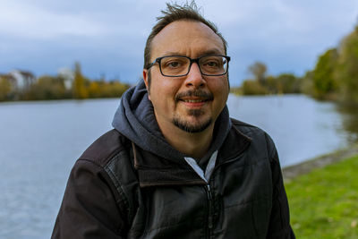 Portrait of man wearing eyeglasses standing against lake