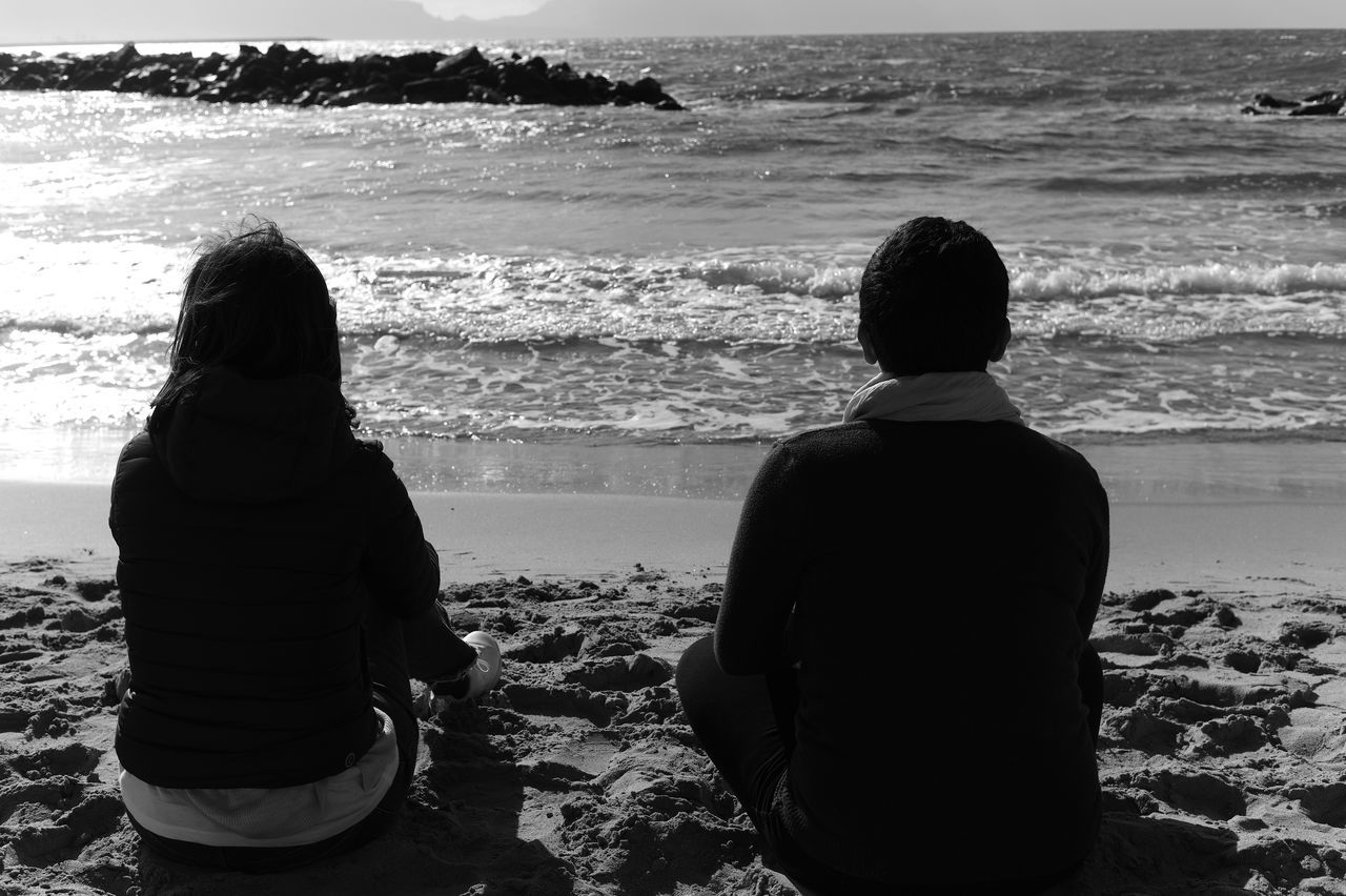 water, sea, beach, land, rear view, two people, black, nature, sky, black and white, togetherness, sitting, adult, leisure activity, men, women, monochrome, horizon over water, beauty in nature, monochrome photography, ocean, horizon, vacation, trip, holiday, scenics - nature, lifestyles, white, child, coast, sand, relaxation, tranquility, family, wave, silhouette, outdoors, shore, tranquil scene, bonding, female, day, emotion, three quarter length, childhood, person