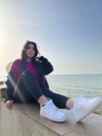 Portrait of young woman sitting on retaining wall infront of the sea 