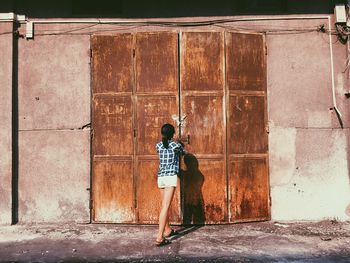 Rear view of woman standing by old rusty closed door