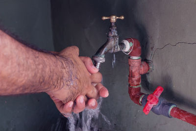 Close-up of hand holding water pipe against wall