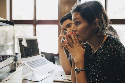 Tensed mid adult businesswoman with hands clasped looking at computer monitor in office