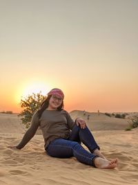 Woman sitting on beach against sky during sunset