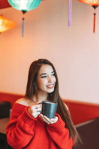 Beautiful smiling young asian woman in red with cup of tea in chinese restaurant