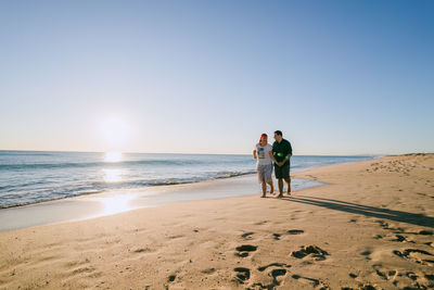 Rear view of friends standing on beach against clear sky