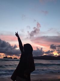 Silhouette woman with arms raised on beach against sky during sunset