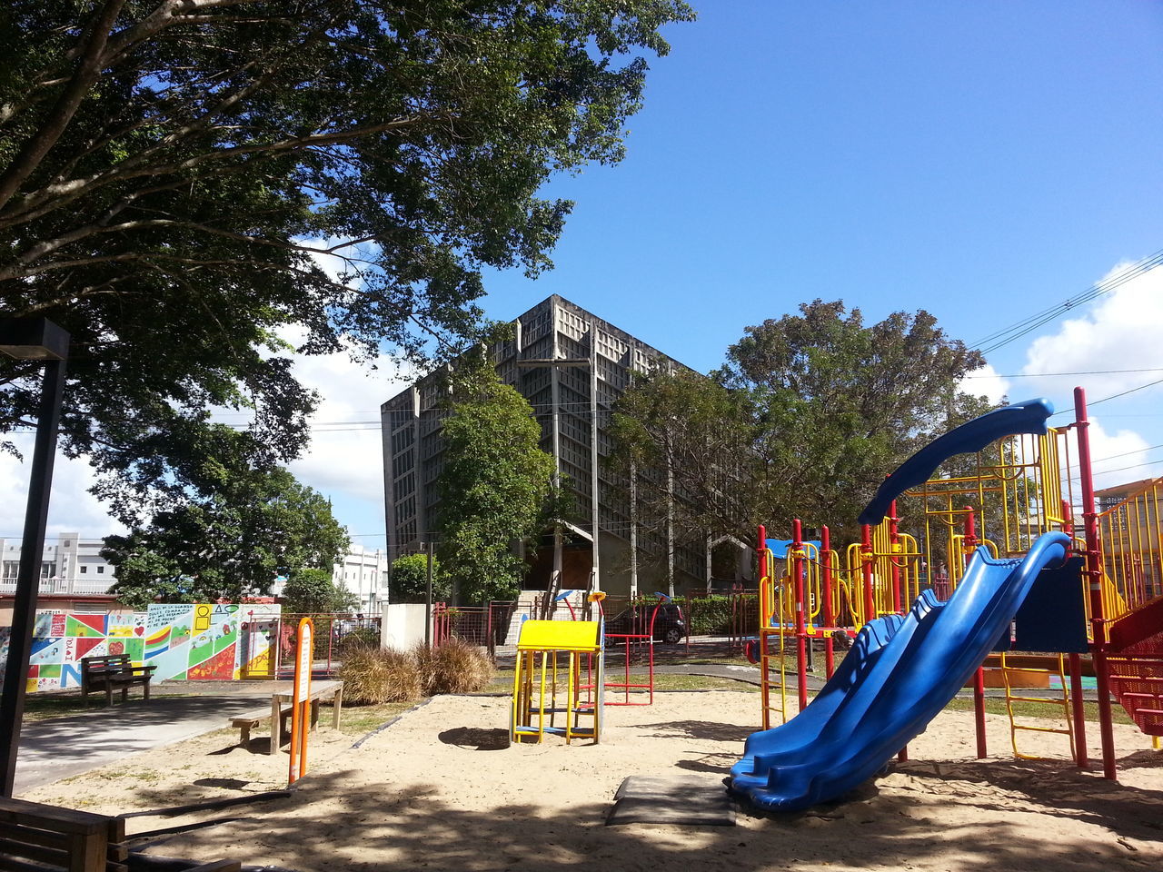 tree, blue, clear sky, playground, built structure, sunlight, beach, park - man made space, sky, architecture, day, fence, shadow, incidental people, outdoors, absence, railing, multi colored, childhood, swing