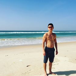 Portrait of shirtless man standing on shore at beach against sky