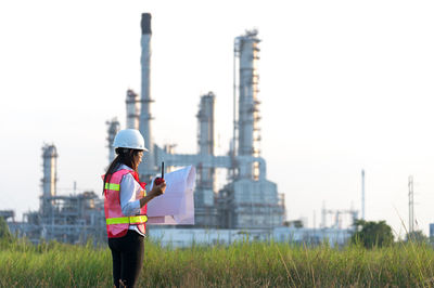 Architect holding blueprint and walkie-talkie while standing at construction site