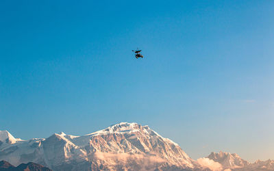 Low angle view of snowcapped mountains against clear blue sky