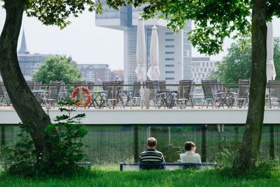 Rear view of man and woman sitting on bench with terrace restaurant in background