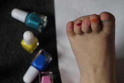 Cropped image of leg by multi colored nail polish bottles on floor