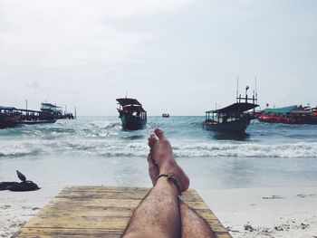 Low section of legs against boats in calm sea