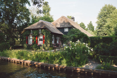 House and trees by lake against sky