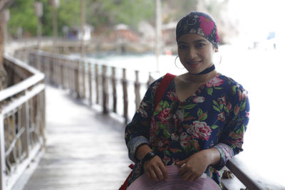 Portrait of smiling young woman standing against railing