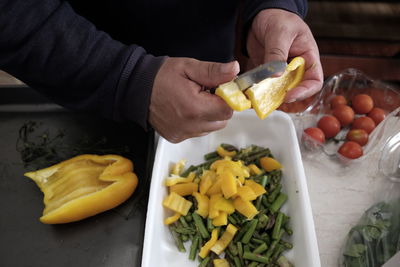 Cropped hand of man chopping yellow bell pepper in kitchen